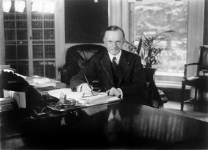 President Coolidge seated at his desk in the Oval Office.
